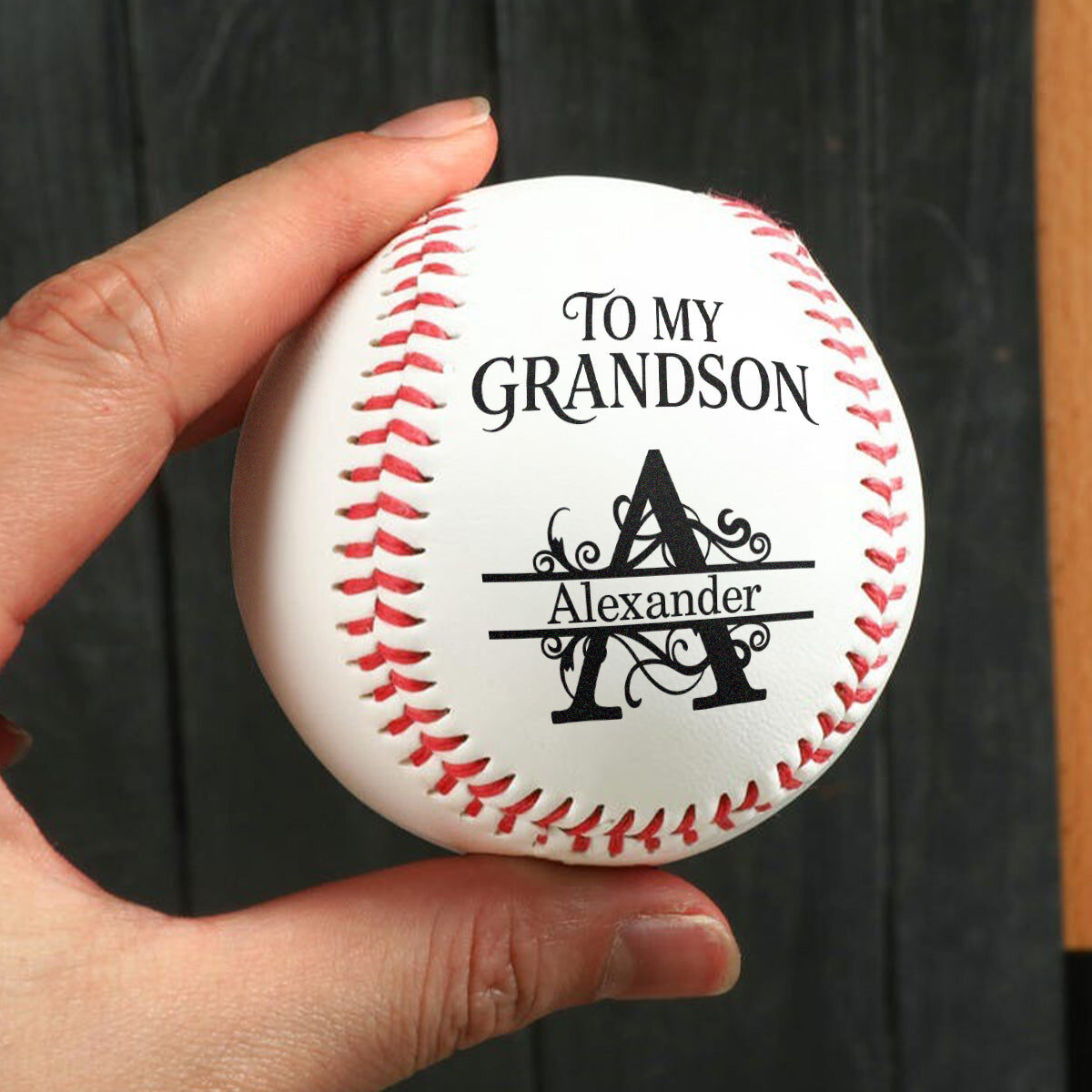 A hand holding the personalized baseball for Alexander, showing the front with To My Grandson above the letter A monogram